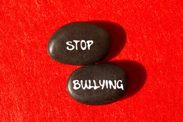 Stop bullying message written on black stones on red background. Conceptual stop bullying symbol....