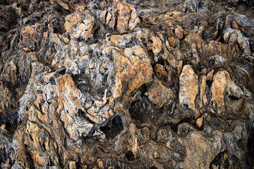 Detailed of a weathered and eroded rock formation, revealing layers of geological history. This abstract stone texture with dark, rugged patterns makes for a powerful grunge, natural background
