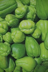 Close-up of a pile of fresh green chayote squashes or Labu Siam in bahasa Indonesia with shiny skin and natural texture. Perfect for organic food, vegetable, or farming themes.