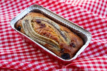 homemade Banana cake topping with banana and cranberry in aluminum foil packaging place on placemat...