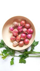 Fresh red shallots in a beige bowl with celery leaves on white background. Ideal for culinary, kitchen, organic food, and healthy lifestyle themes.