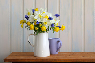Spring flowers bouquet in white jug decorating wooden table