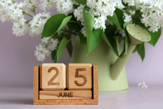 Wooden perpetual calendar showing june 25 with white lilac flowers in watering can