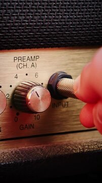 Hand plugging jack cable into music guitar amplifier, close up. Vertical video