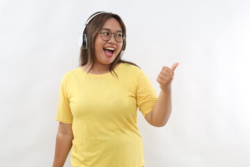 Young asian woman listening to music isolated on white background points with thumb finger away, laughing and carefree.