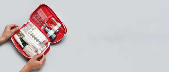 Female hands with first aid kit and pills on grey background