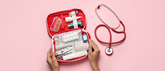 Naklejka na ściany i meble Female hands with first aid kit and pills on pink background
