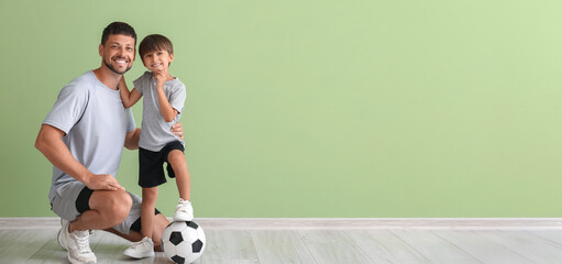 Little boy with soccer ball and trainer near green wall