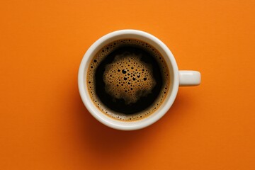 Freshly brewed coffee in a white cup against a vibrant orange background