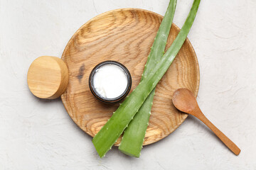 Wooden plate with jar of cosmetic product and aloe vera leaves on grey background