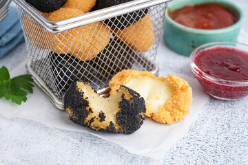 Metal basket with different delicious fried mozzarella balls and sauces on light background, closeup