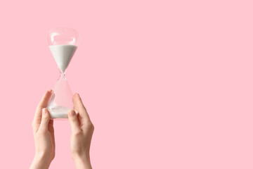 Female hands holding hourglass on pink background