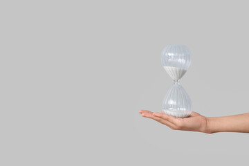 Female hand holding hourglass on grey background