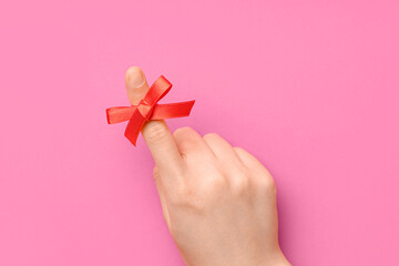 Female hand with red bow on index finger against pink background. Reminder concept
