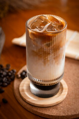 A tall glass of iced latte with visible milk and espresso layers, surrounded by scattered coffee...