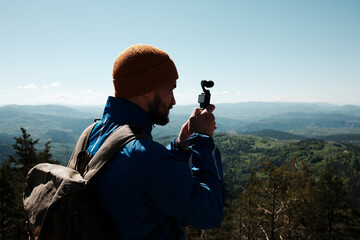 Man filming scenic mountain view with a compact gimbal camera on a sunny spring day in Zlatibor,...