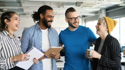 Four young adults of different ethnic backgrounds share ideas and laugh together in a bright, contemporary office. They hold notebooks and enjoy each other's presence during this collaborative moment