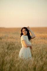 A young brunette walks in wheat fields at sunset in summer. Growing organic wheat and barley.