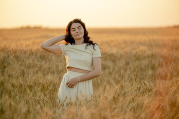 A young brunette walks in wheat fields at sunset in summer. Growing organic wheat and barley.