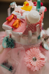 Close-up of pink baby shower diaper cake decorated with baby socks, rubber duck, tulle, and pastel accessories including a flower embellishment and infant care items