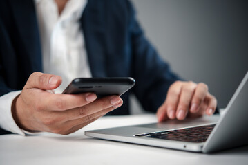 Close-up of hands holding smartphone working on laptop, business technology, digital communication, online collaboration, email, or remote management.