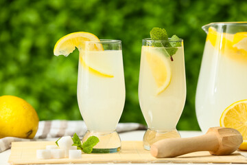 Glasses and jug of fresh lemonade with mint on white wooden table outdoors