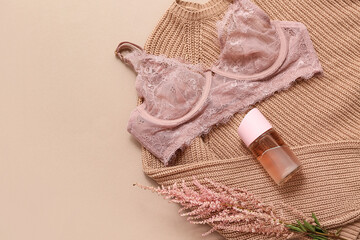 Composition with stylish lace bra, knitted sweater, bottle of perfume and flower on color background