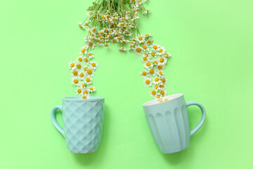 Cups and chamomile flowers on green background. Top view