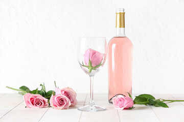 Bottle of pink wine with glass and beautiful roses on white tile table
