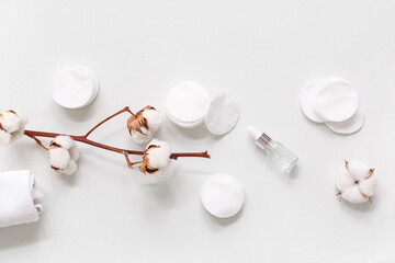 Composition with cosmetic pads, bottle of essential oil and cotton branch on light background
