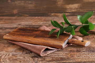 Empty cutting board with napkin and ruscus leaves on wooden table
