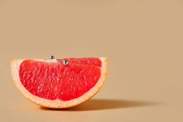 Piece of grapefruit with piercing on beige background