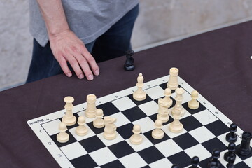 A person is making a move with the white king during a chess game. The board shows an intense...