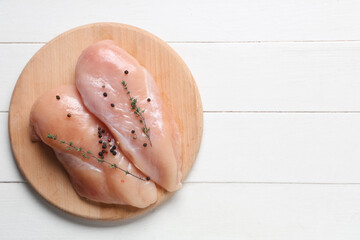 Board with raw chicken breast, thyme and peppercorns on white wooden background