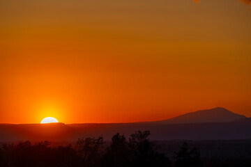 Obraz premium Bright orange sunset over mountains creating silhouettes of trees