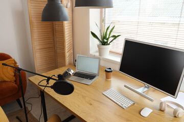 Workplace with blank laptop, computer monitor and microphone in recording studio