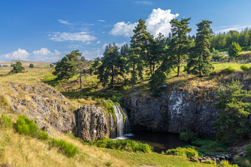 Waterfall cascading down rocky cliff in French countryside near Saint Sulpice les Champs, Creuse, France