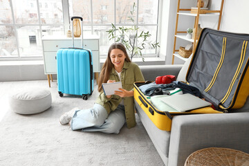 Female tourist making checklist while packing suitcase at home