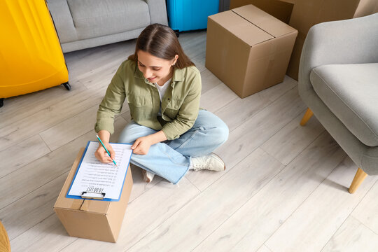 Young woman making checklist in room on moving day