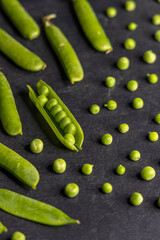 Fresh green peas arranged on dark background showing pods and single peas