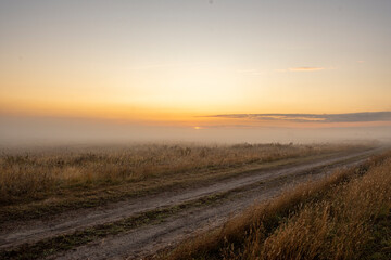 Calm foggy landscape of empty agricultural meadow in countryside in the morning with golden light from rising sun