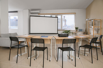 Interior of empty classroom with blank projector screen and desks
