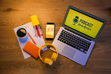 Laptop, mobile phone with podcast and headphones on table, top view