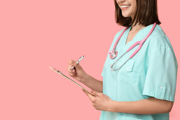 Happy female cardiologist with stethoscope and clipboard on pink background, closeup