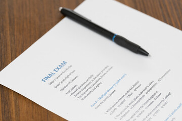 High school final exam in general knowledge placed on a wooden desk. The paper includes questions related to planets, geography and science alongside exam instructions. A pen rests above the sheet