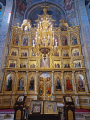 Obraz premium Capriana Monastery indoors view of traditional ornate Christian Orthodox church located in Moldova. Scene during divine service with a monk praying at the altar underneath a grand gilded chandelier