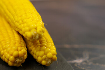 Three yellow ears of corn lie on a dark background with space for text. The concept of healthy nutrition, natural iron, corn cultivation. High quality photo