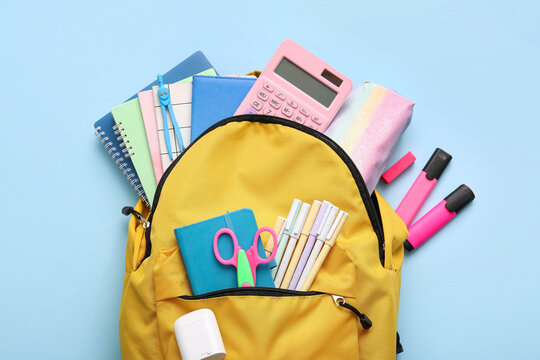 Yellow school backpack with different stationery supplies on blue background - Powered by Adobe