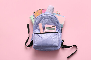 Lilac school backpack with different stationery supplies on pink background