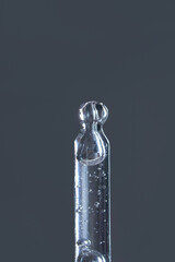 Transparent glass dropper with air bubbles against a dark gray background.